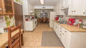 A compact kitchen with white cabinets, a wooden chair, a dining table, and a refrigerator.