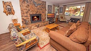 A cozy living room with a stone fireplace, a sofa, a patterned rug, and a wooden coffee table.