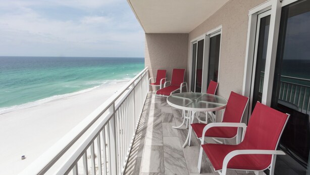 A balcony with a glass table and red chairs, overlooking a beach with clear turquoise water. - D1005 Direct Gulf View, 3 Pools, Tennis and Pickle Ball (Panama City Beach)