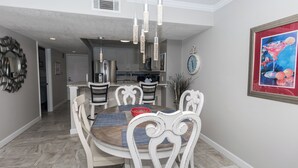 A dining area with a round table, white chairs, and pendant lights. - D1005 Direct Gulf View, 3 Pools, Tennis and Pickle Ball (Panama City Beach)