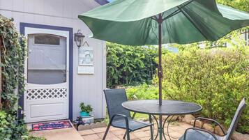 A patio with a round table and chairs, a green umbrella, and a white door with a window.