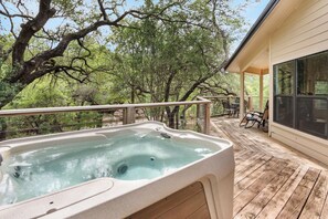 Ein Whirlpool auf einer Holzterrasse mit Blick auf Bäume und ein Gebäude.