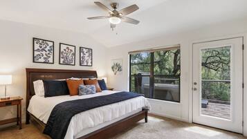 A bedroom with a large bed, a ceiling fan, a window with a view of the outdoors, and framed artwork on the wall.