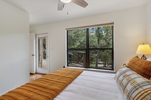Une chambre avec une grande fenêtre, un ventilateur de plafond et un lit recouvert d’une couverture à rayures.
