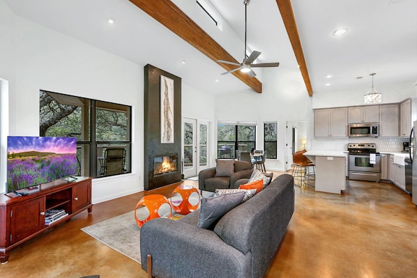A spacious living room with a fireplace, a large TV, and a dining area with a kitchen in the background.