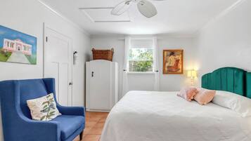 A bedroom with a bed, a chair, a wardrobe, a ceiling fan, a window, and a painting.