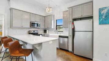 A modern kitchen with white cabinetry, stainless steel appliances, and a central island with bar stools.