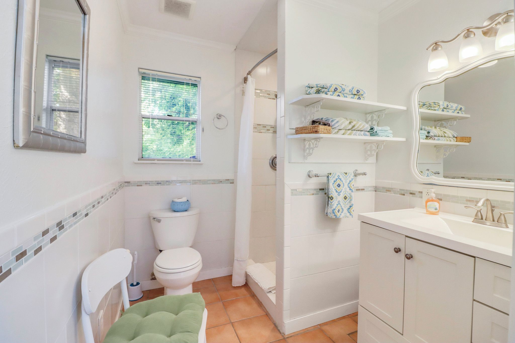 A bathroom with a toilet, shower, and sink. There is a window and a mirror above the sink.