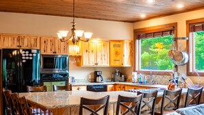 Une cuisine avec des meubles en bois, un grand îlot central doté de chaises, des appareils électroménagers en acier inoxydable et une vue sur la verdure par la fenêtre.