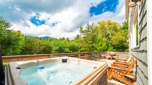 Un bain à remous sur une terrasse en bois, avec vue sur une forêt et des montagnes.