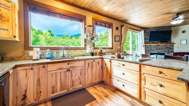 Une cuisine spacieuse dotée de meubles en bois, de plans de travail en granit et de grandes fenêtres offrant une vue sur la verdure.