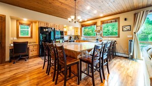 Une cuisine spacieuse avec des meubles en bois, un grand îlot central doté de tabourets de bar et une vue sur l’extérieur grâce à de grandes fenêtres.