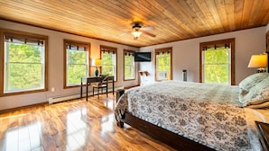 Une chambre avec un plafond en bois, de grandes fenêtres, un lit, un bureau et une chaise.