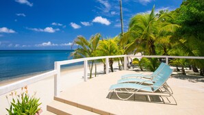 A beachside patio with lounge chairs, palm trees, and a view of the ocean. - 2 bedroom beachfront in West End with amazing sunset view (Roatan)