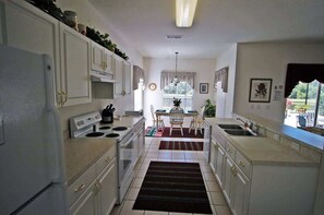 A kitchen with white cabinets, a stove, and a dining area with a table and chairs. - Lakefront Pool Villa w/ Game Room, Near Disney (Kissimmee)