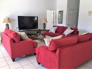 Uma sala de estar com sofás vermelhos, uma TV de tela plana, duas luminárias e uma mesa de centro.