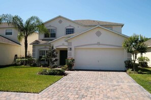 A two-story house with a garage, a paved driveway, and a well-maintained lawn. - Lakefront Pool Villa w/ Game Room, Near Disney (Kissimmee)