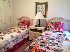 Quarto com duas camas de solteiro, cada uma com roupa de cama florida, uma mesinha de cabeceira com abajur e um quadro na parede.