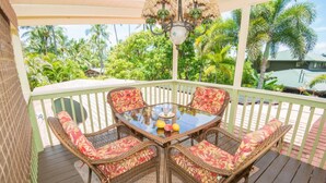 Un espace extérieur aménagé, abrité et doté de mobilier en osier et d’une table en verre, entouré d’une clôture blanche et de palmiers.