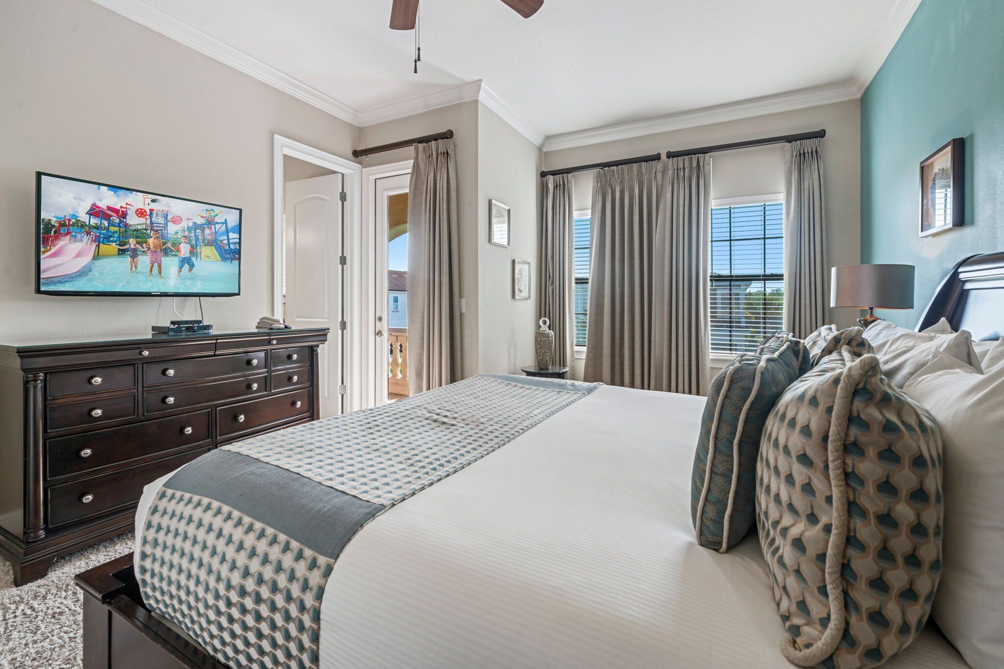 A hotel room with a large bed, a dresser, a television, and a window with curtains.