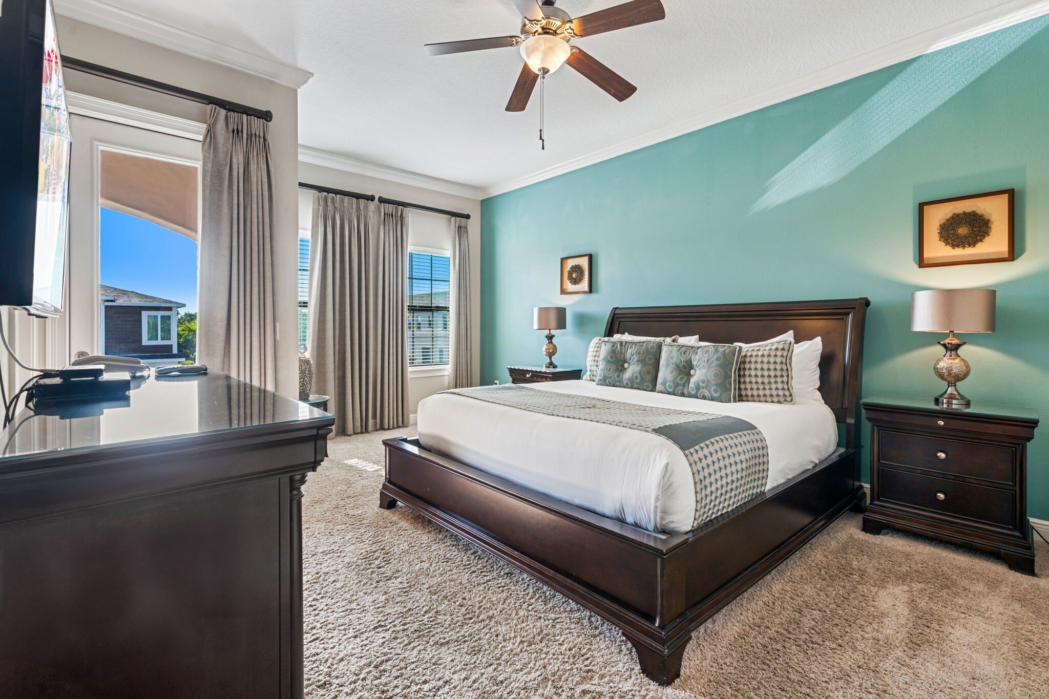 A bedroom with a large bed, a ceiling fan, a nightstand, and a desk.