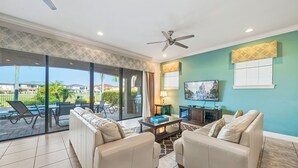 A spacious living room with a large sliding glass door leading to a patio area, a ceiling fan, and a television on the wall. - Fairway Pinehurst: Theater, Pool, Water Park, Golf View, Near Disney (Kissimmee)