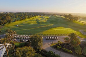 A golf course with a parking area, palm trees, and a distant view of a city skyline. - Fairway Pinehurst: Theater, Pool, Water Park, Golf View, Near Disney (Kissimmee)