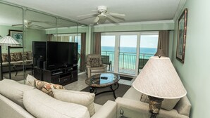 Ein Wohnzimmer mit Fernseher, Sofa, Sesseln und einem Balkon mit Meerblick.