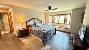 Un dormitorio con cama, mesitas de noche, ventilador de techo, ventana con vistas y televisor.