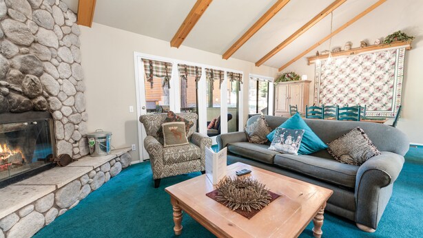 A cozy living room with a stone fireplace, a wooden coffee table, a grey sofa with blue cushions, and a patterned wall.