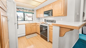 A compact kitchen with wooden cabinets, a microwave, a stove, and a dishwasher.