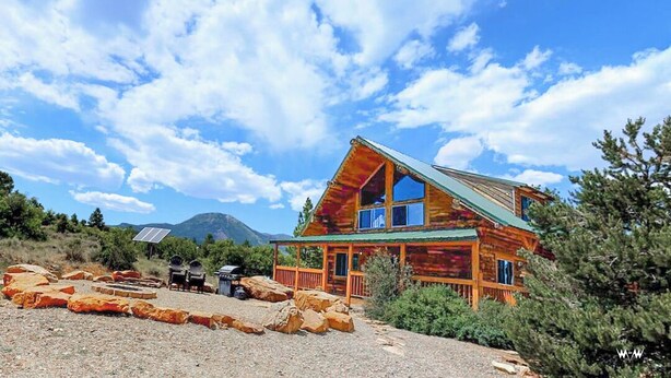 A rustic cabin with a green roof, surrounded by rocks and greenery, with mountains in the background. - W-W: Guest Ranch Group Lodging up to 70! (Monticello)