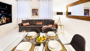 Una sala de estar moderna con un sofá, una mesa de comedor preparada para cuatro comensales y un espejo grande en la pared.