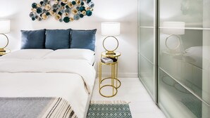 Un dormitorio moderno con una cama grande, dos mesitas de noche con lámparas, un adorno de pared y una alfombra estampada.