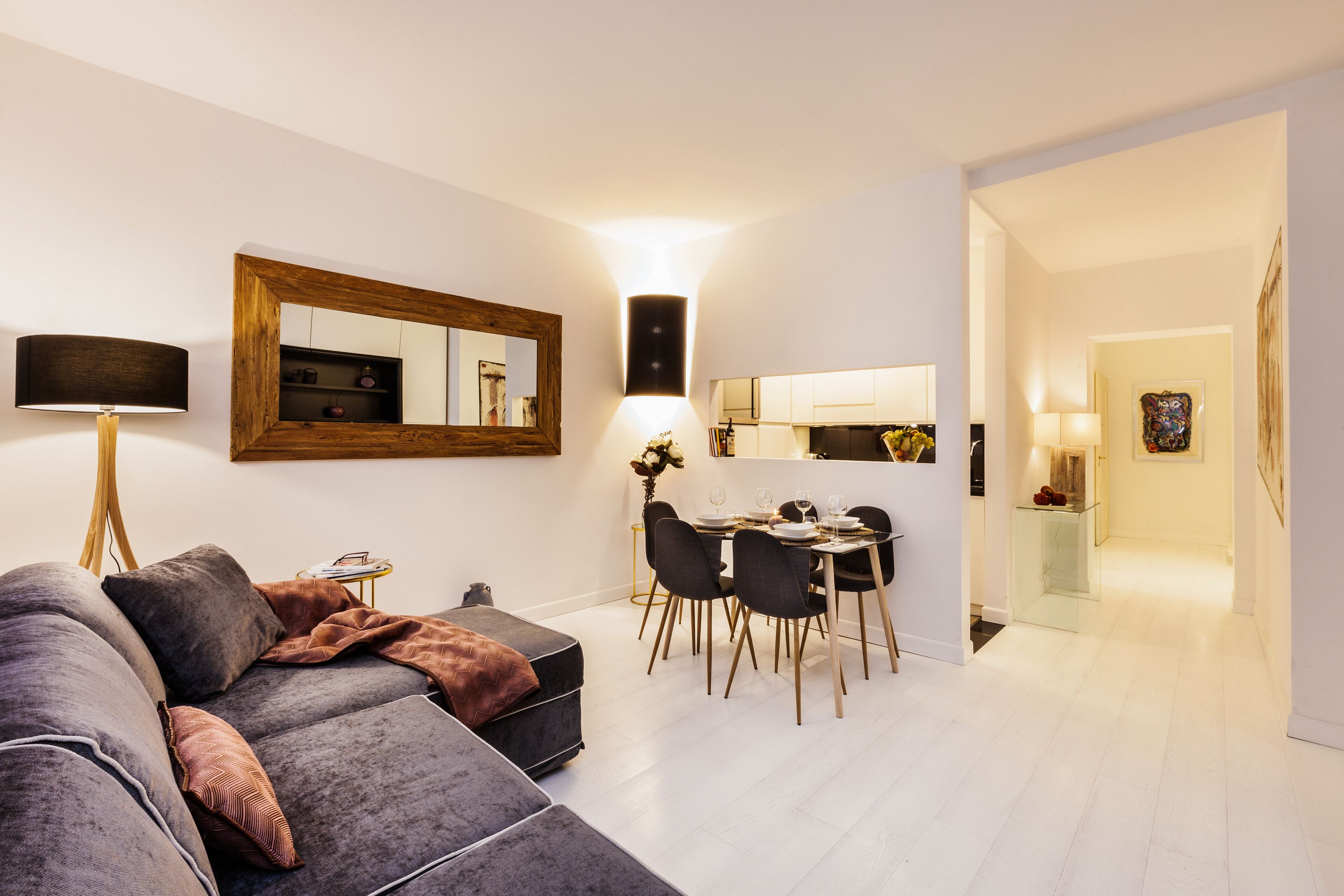 Una sala de estar moderna con un sofá modular gris, un comedor con mesa de vidrio, y una cocina al fondo.
