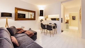 Una sala de estar moderna con un sofá modular gris, un comedor con mesa de vidrio, y una cocina al fondo.