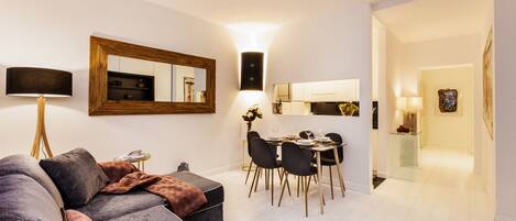 Una sala de estar moderna con un sofá modular gris, un comedor con mesa de vidrio, y una cocina al fondo.