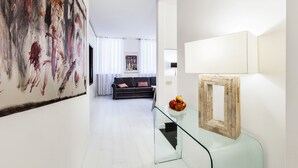 Una sala de estar moderna con una mesa de centro de vidrio, un sofá negro y un cuadro abstracto de gran tamaño en la pared.