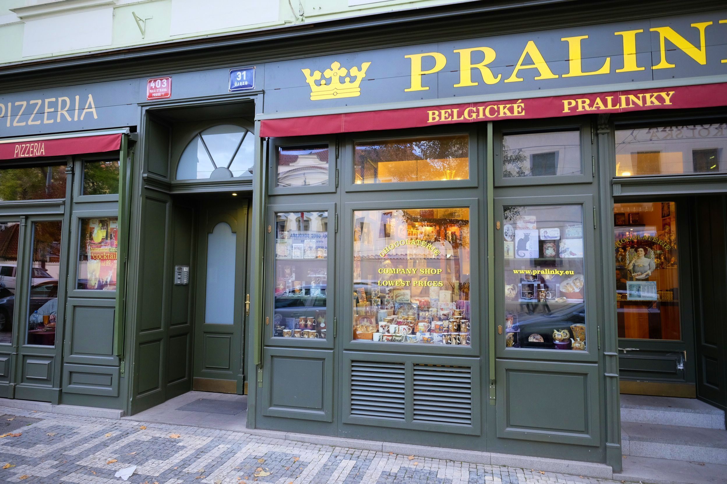 Una fachada con un letrero que dice 'PRALINKY' y 'BELGICKE PRALINKY', indicando una tienda que vende chocolates y otros productos.