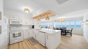 Una cocina moderna con armarios blancos, una isla central y un comedor con vista al océano.