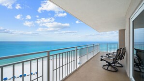 Un balcón con vista al océano y a la playa, con una silla y una mesa.
