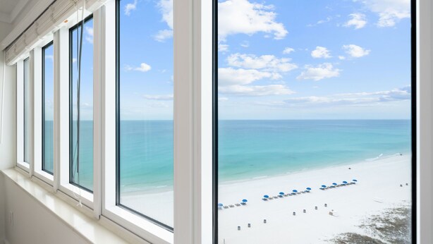 Vista de una playa a través de una ventana, con cielo despejado y mar tranquilo.