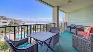 Een balkon met een tafel en stoelen, een comfortabele zithoek en uitzicht op het strand en de oceaan.