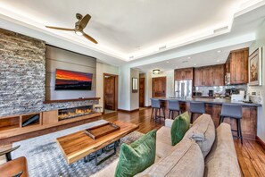 A modern living room with a stone fireplace, wooden furniture, and a large TV.