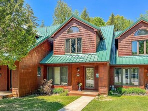 A two-story wooden house with a green roof, large windows, and a well-maintained lawn.