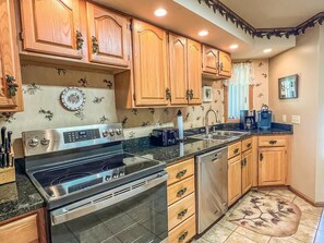 A kitchen with wooden cabinets, a stainless steel stove, a dishwasher, and a granite countertop.
