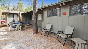 Un espace patio avec une table et des chaises, un arbre et un bâtiment doté de fenêtres et d’une porte.