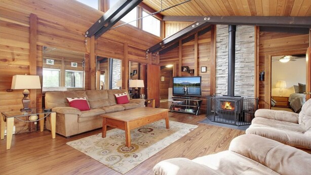 L’intérieur d’une cabane en rondins, avec un canapé, un fauteuil, une télévision, une cheminée et un plancher en bois.