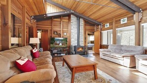 L’intérieur d’une cabane en rondins, avec une cheminée, deux canapés, une table basse et un téléviseur.