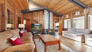 A log cabin interior with a fireplace, two sofas, a coffee table, and a television.